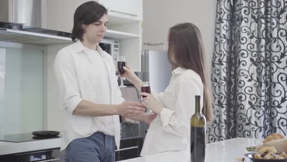 Young Brunette Woman Taking Wine in Glasses, Happy Romantic Couple Clinking and Kissing in Kitchen