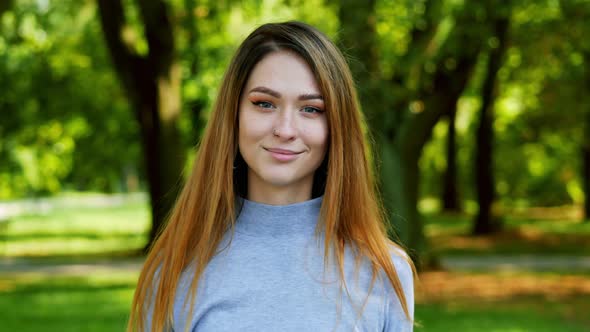 Portrait of Cheerful Beautiful Woman with Red Hair Looking at Camera at Sunny Park