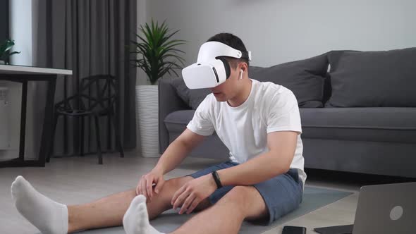 Young Man in Virtual Reality Glasses Performs the Stretching of the Muscles Sports Using Modern