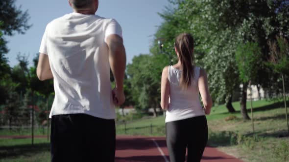 Cheerful Beautiful Woman Encouraging Man To Run Faster on Running Track Outdoors. Joyful Caucasian