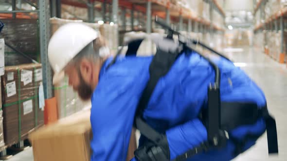 Warehouse Employee in Ergoskeleton is Lifting a Box and Walking Away