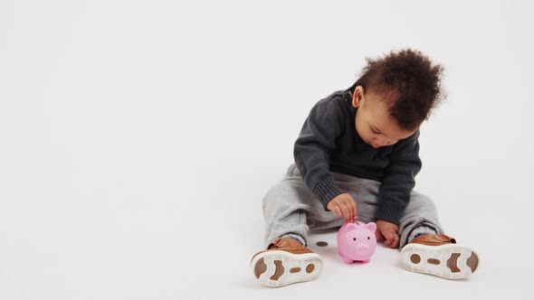 Lovely African American Curled Little Boy Sitting on the Floor Looking at the Pink Toy Pig Studio