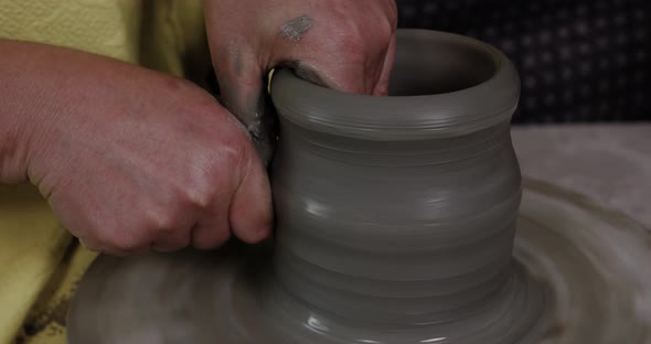 Hands work the pottery on the lathe.