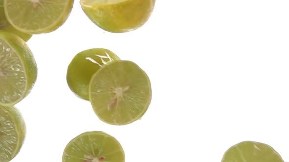 Closeup of the Halves of Green Limes Falling Diagonally on the White Background