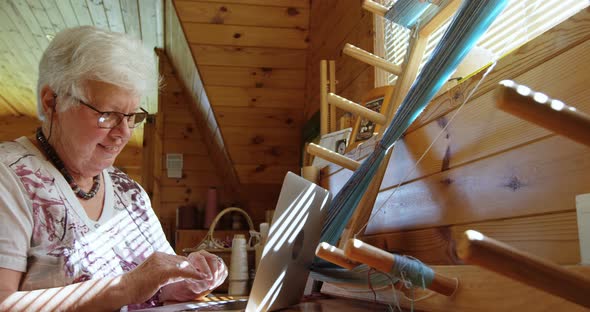 Side view of old caucasian senior woman working on laptop and sitting at desk in workshop 4k