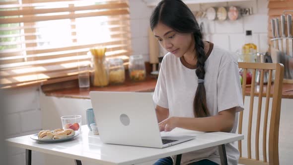 Young asian woman happy smiling using laptop in kitchen at home.