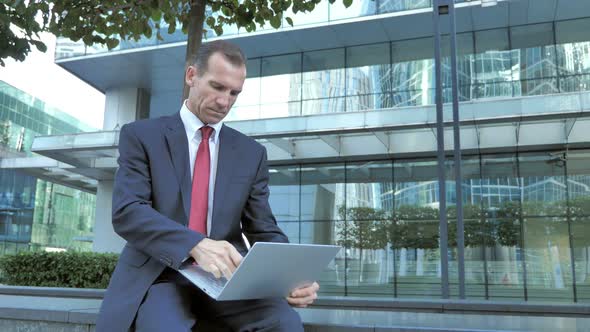 Online Shopping By Businessman on Laptop Outside Office