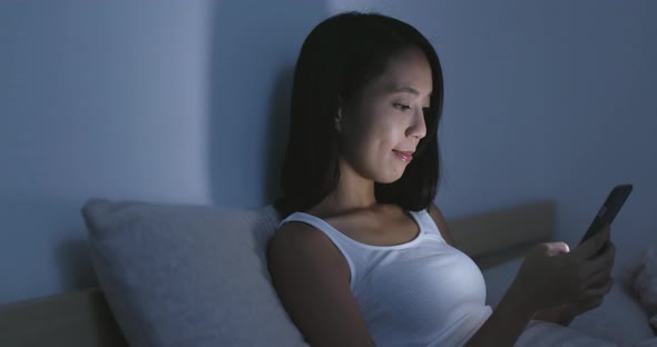 Woman looking at cellphone on bed