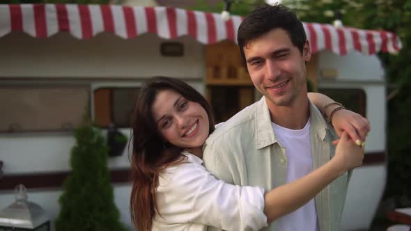 Portrait of Romantic Couple Man and Woman Smiling While Hugging Near House on Wheels Outdoors