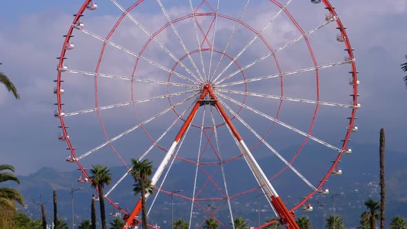 Ferris Wheel Against the Blue Sky with Clouds Near the Palm Trees in the Resort Town, Sunny Day
