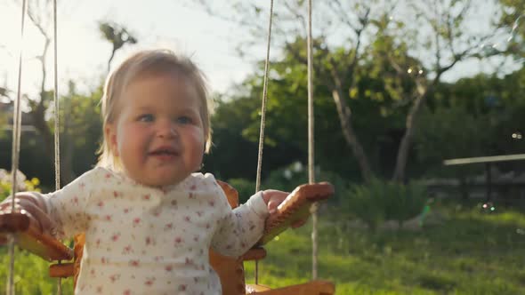 Portrait of smiling caucasian baby having fun on a swing, looking at flying soap bubbles.