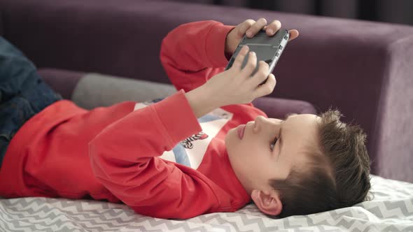 Boy Playing Mobile Game on Smartphone on Sofa. Kid Playing Mobile Phone