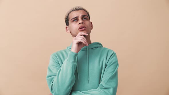 Concentrated curly-haired man wearing blue hoodie thinking