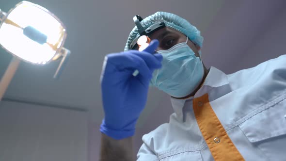 Concentrated Professional Dentist Adjusting Dental Headlight Leaning to Camera with Instruments