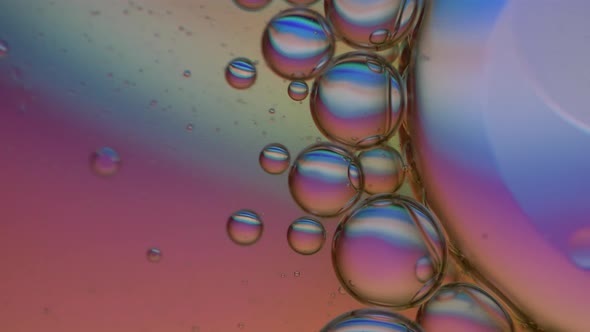 Oily bubbles changing color in water. Drops of oil mixing underwater. Close up macro shot.