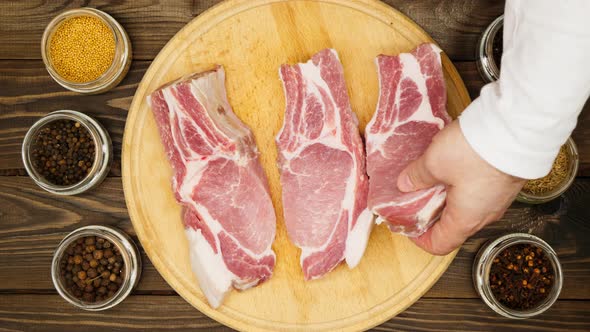 The cook prepares pieces of meat on a cutting board on a wooden table. A man's hand lays out a pork