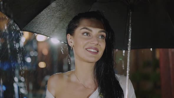 Happy Brunette Stands with Umbrella Under the Rain and Smiles