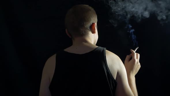 A Man Sits Back and Smokes a Cigarette on a Black Background, Nicotine and Health