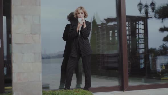 Beautiful Woman in Black Suit Drinks a Cup of Beverage and Poses at Home