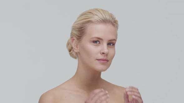 Studio portrait of young, beautiful and natural blond woman applying skin care cream. F