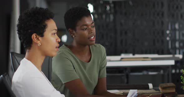 Two diverse businesswoman talking, working together on laptop in office