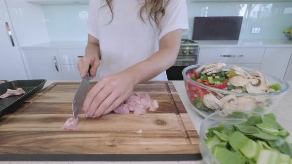 Wide angle sliding shot of woman in kitchen preparing chicken and vegetables for asian stir fry