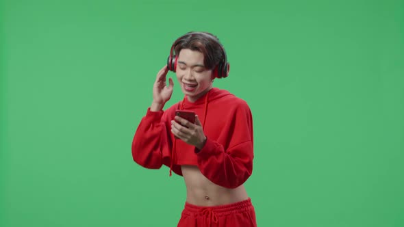 Transgender Male With Headphones Listening To Music From Mobile Phone And Dancing On Green Screen