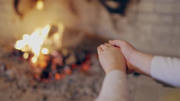 Close-up footage of young woman warming cold hands at burning fireplace.