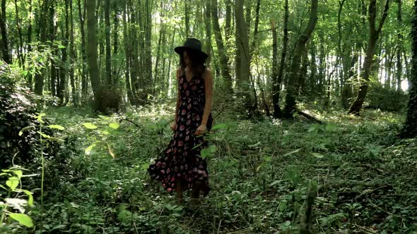 Young, trendy woman in long dress twirls in the middle of a forest