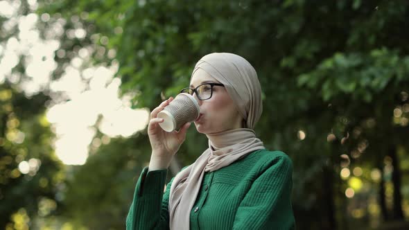 Young Muslim Woman Wearing Hijab Head Scarf and Coffee to Go in City Park