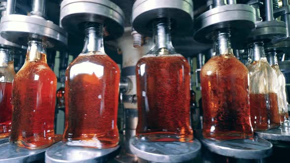 Revolving Machine Is Filling Glass Bottles with Alcoholic Beverage