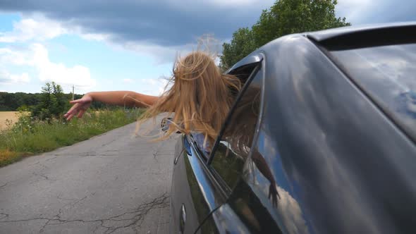 Carefree Little Girl Leaning Out of Car Window and Waving Her Hand in Wind While Riding Through