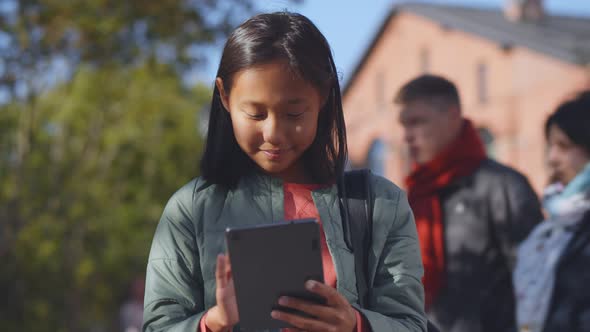 Happy Asian Girl Student with Backpack Using Digital Tablet Standing Outdoors School Building