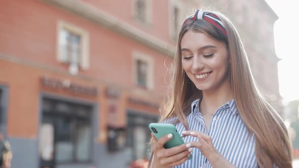 Smiling Young Woman Wearing in Blue and White Striped Dress Shirt Using Smartphone Standing on the