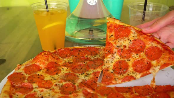 Girls Hand Takes a Slice of Pepperoni Pizza on the Background of Bubbling Hookah and Cocktails in a