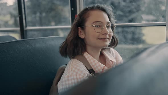 Smiling School Girl Sitting at Bus Window in Glasses