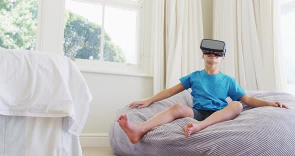 Caucasian boy wearing vr headset while sitting on the bean bag at home