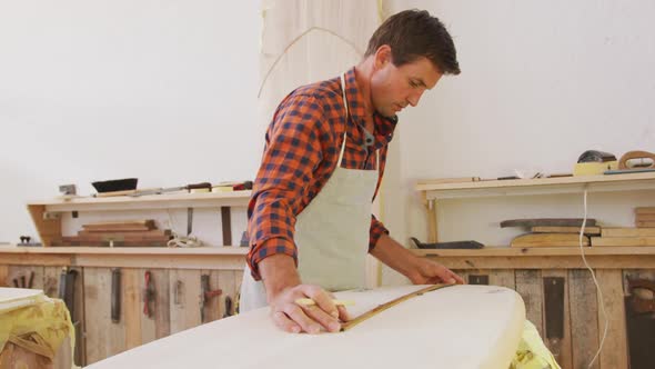 Caucasian male surfboard maker checking a surfboard after polishing