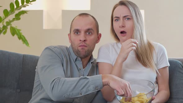 A Couple Watches a Scary Movie on the Couch While Eating a Snack