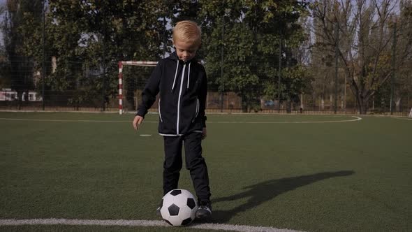 A Small Sevenyearold Boy Trains with a Soccer Ball on a Soccer Field