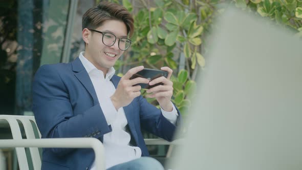 Close-up of a attractive asian man sitting on bench playing game online