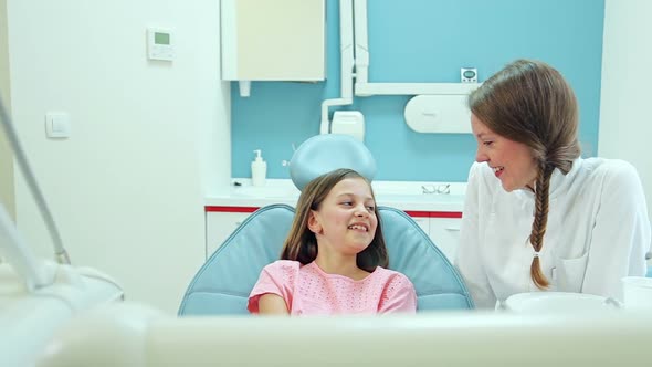 Smiling female dentist talking with lovely little girl