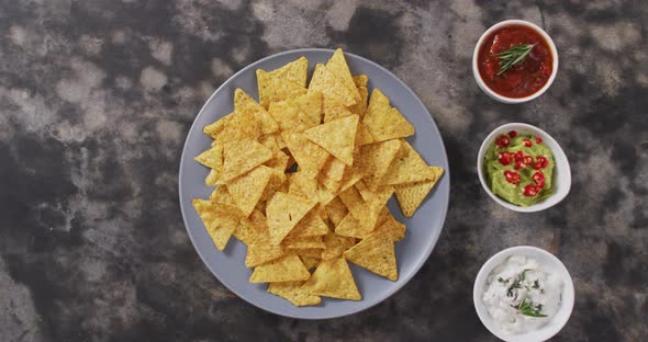 Close up of nachos in a plate and sauces on black surface