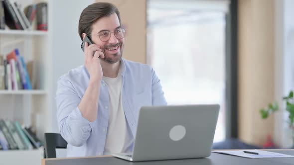 Man in Glasses with Laptop Talking on Smartphone