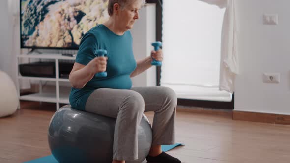Senior Adult Training with Dumbbells and Sitting on Toning Ball