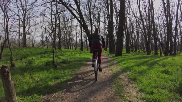 Young Woman on a Bicycle Rides Along a Path in the Forest in a Sunny Spring Day