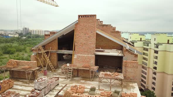 Aerial view of unfinished brick apartment building with wooden roof structure under construction.