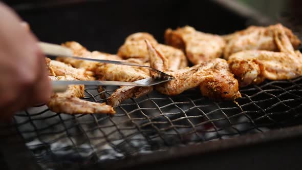 Man Using Metal Tongs To Turning Chicken Wings Which Are Being Grilled on Barbecue