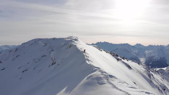 Drone flies towards snowboarder walking on thin ridge in Austria to get first tracks