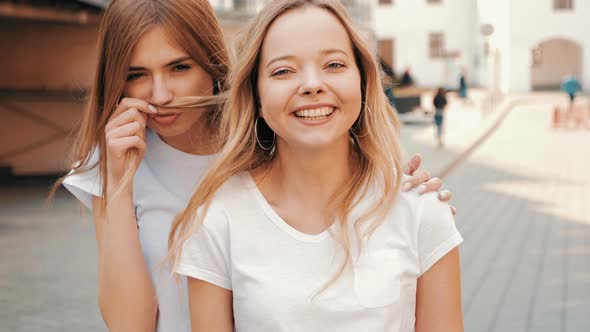 Two young beautiful blond smiling hipster girls in trendy summer clothes